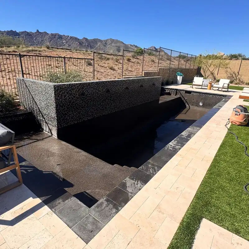 Raised spa wall in black mosaic tile beside a travertine deck