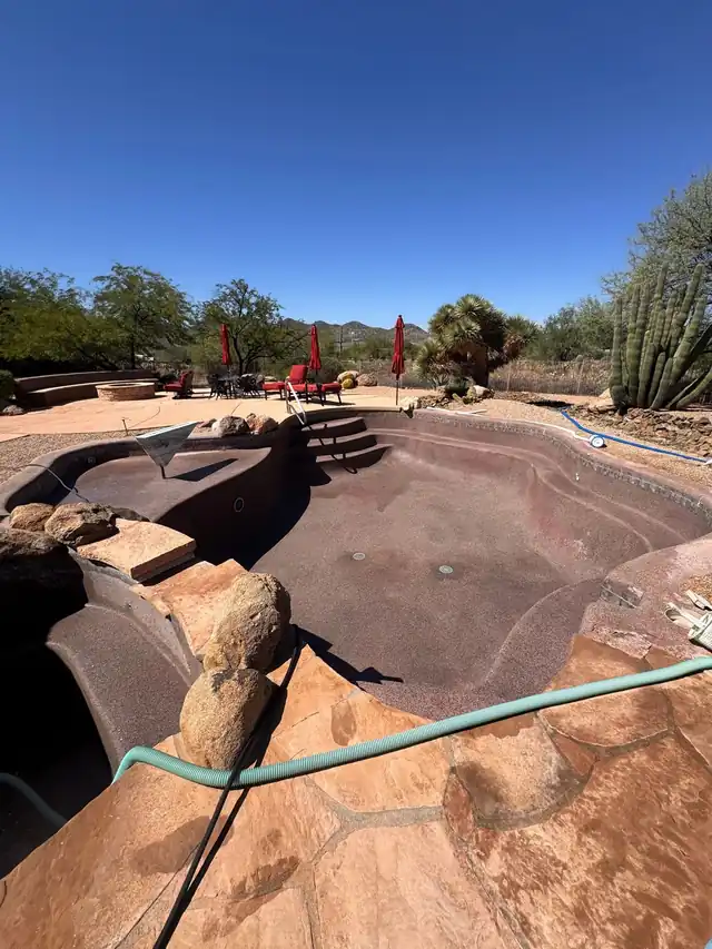 Drained pool and spa shell with a hose across the deck