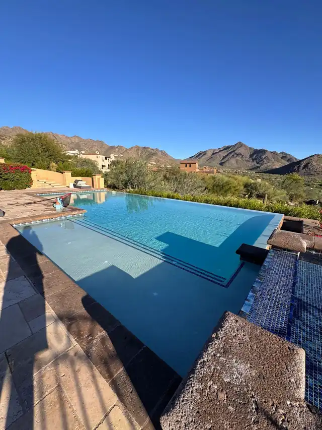 Infinity pool with a blue-tile step and a rock ledge, mountains behind