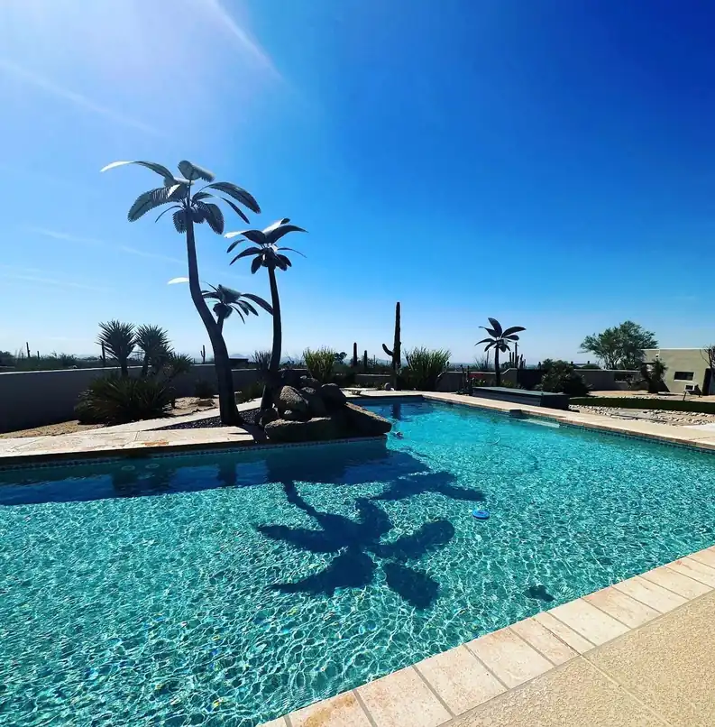 Steel palm-tree sculpture casting its shadow across the pool floor
